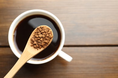 Photo of Spoon with instant coffee above cup of hot drink on wooden table, top view. Space for text