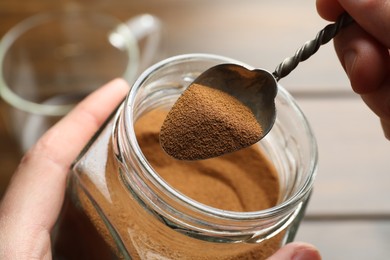 Photo of Woman taking instant coffee from jar on blurred background, closeup