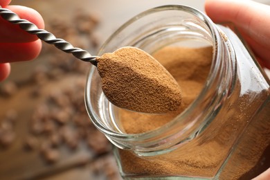 Photo of Woman taking instant coffee from jar on blurred background, closeup