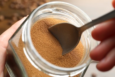 Photo of Woman taking instant coffee from jar on blurred background, closeup