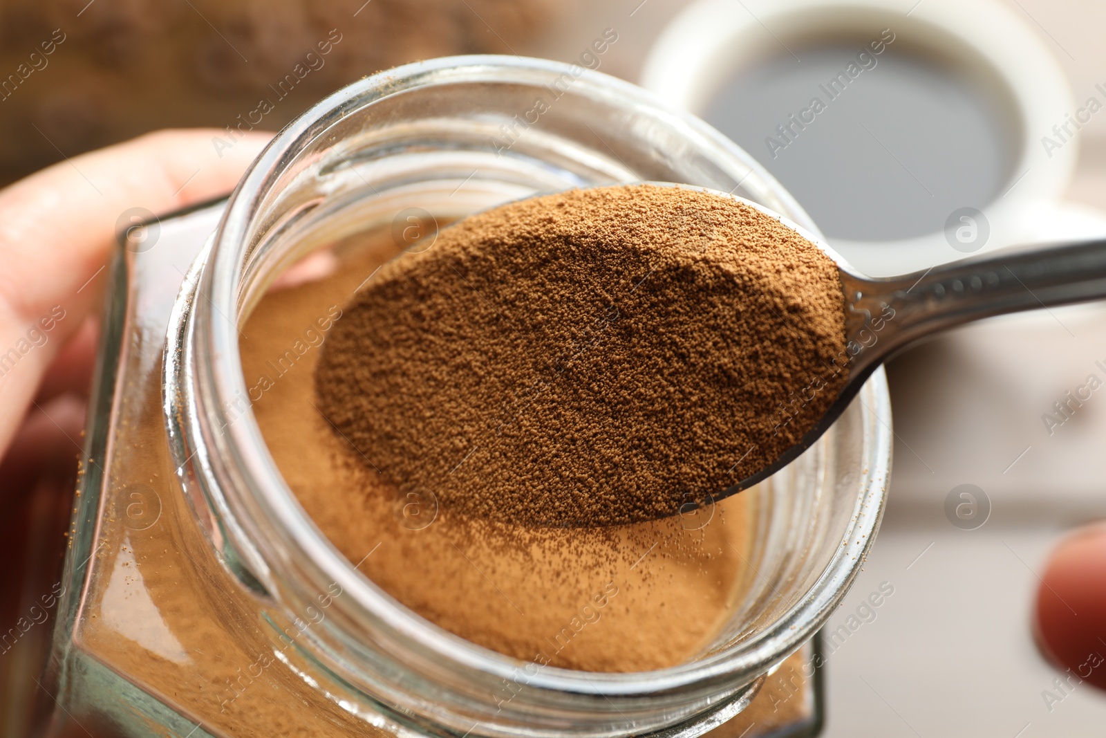 Woman taking instant coffee from jar on blurred background, closeup Photo of Woman taking instant coffee from jar on blurred background, closeup