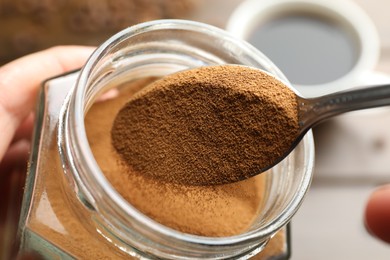 Photo of Woman taking instant coffee from jar on blurred background, closeup