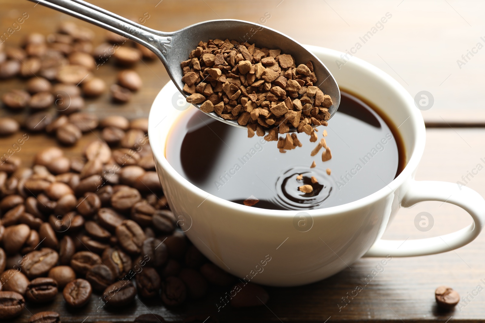 Putting instant coffee into cup of hot drink at wooden table, closeup Photo of Putting instant coffee into cup of hot drink at wooden table, closeup