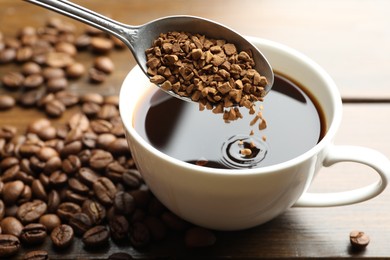 Photo of Putting instant coffee into cup of hot drink at wooden table, closeup