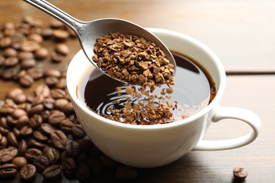 Photo of Putting instant coffee into cup of hot drink at wooden table, closeup