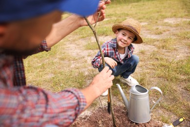 Photo of Father and his son planting tree into soil outdoors, closeup