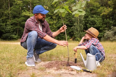 Photo of Father and his son planting tree into soil outdoors