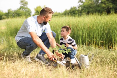 Photo of Father and his son planting tree into soil outdoors