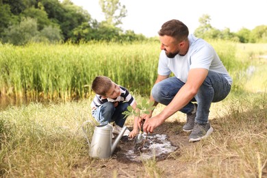 Photo of Father and his son planting tree into soil outdoors