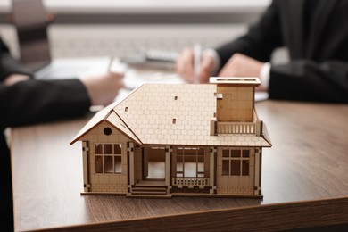 Photo of Real estate agent working with client at desk in office, focus on house model