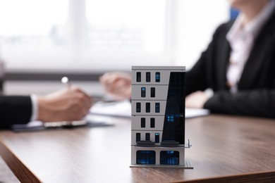 Photo of Real estate agent working with client at desk in office, focus on house model