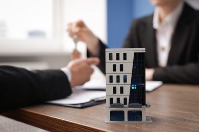 Photo of Real estate agent giving key to client at desk in office, focus on house model