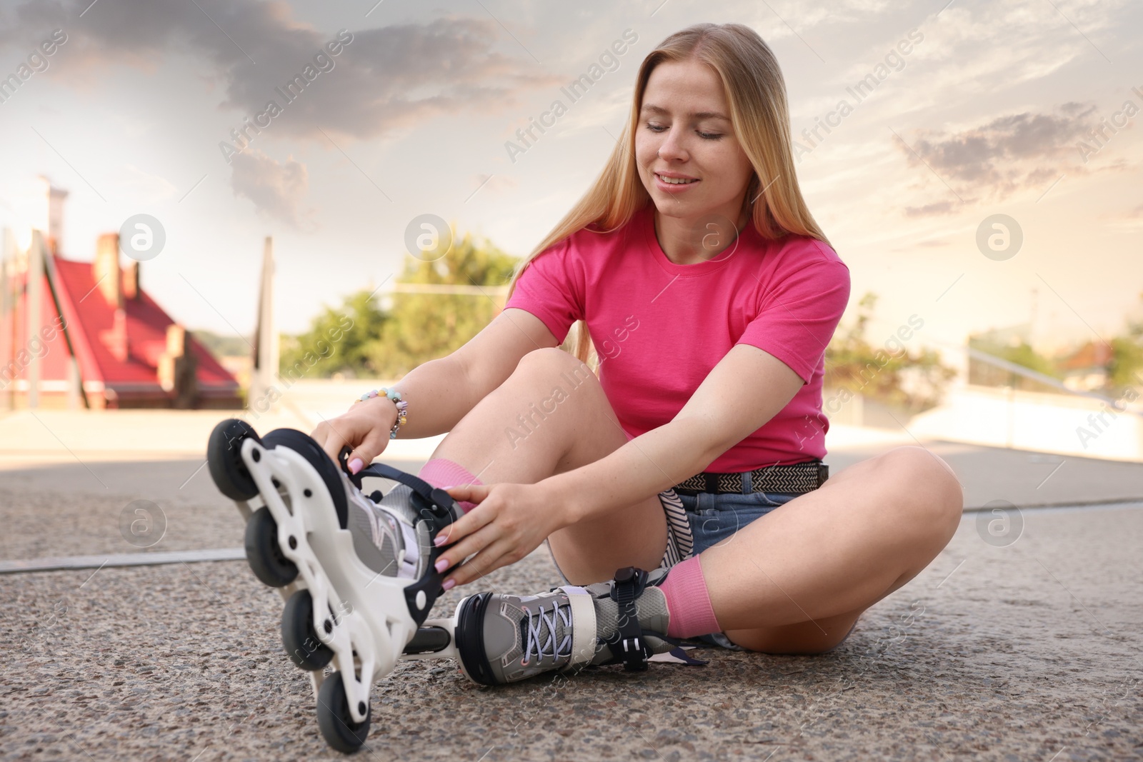 Happy woman putting on roller skates outdoors Photo of Happy woman putting on roller skates outdoors