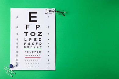 Photo of Vision test chart, glasses, lenses and tweezers on green background, flat lay. Space for text