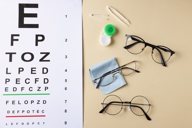 Photo of Vision test chart, glasses, tweezers, cleaning cloth and lenses on beige background, flat lay