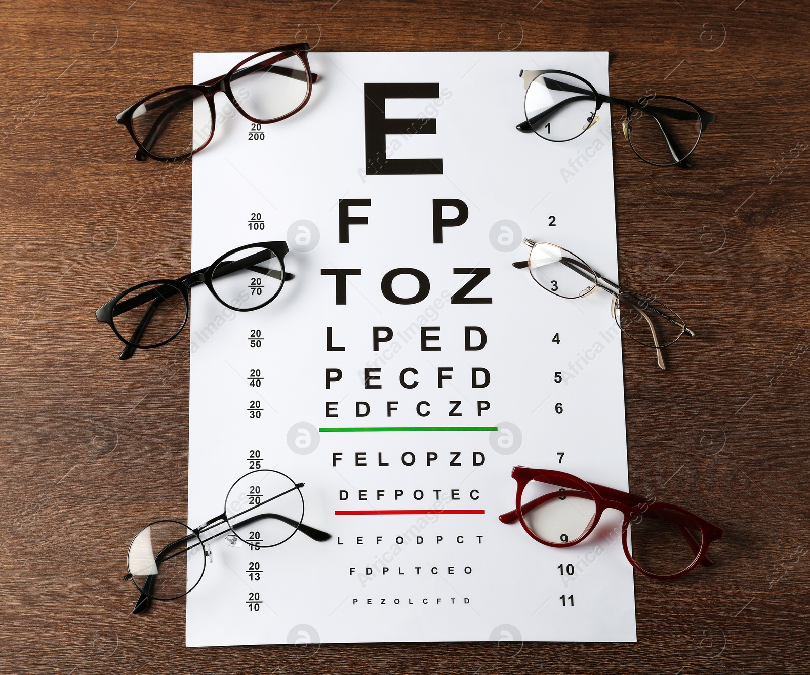 Photo of Vision test chart and glasses on wooden table, flat lay