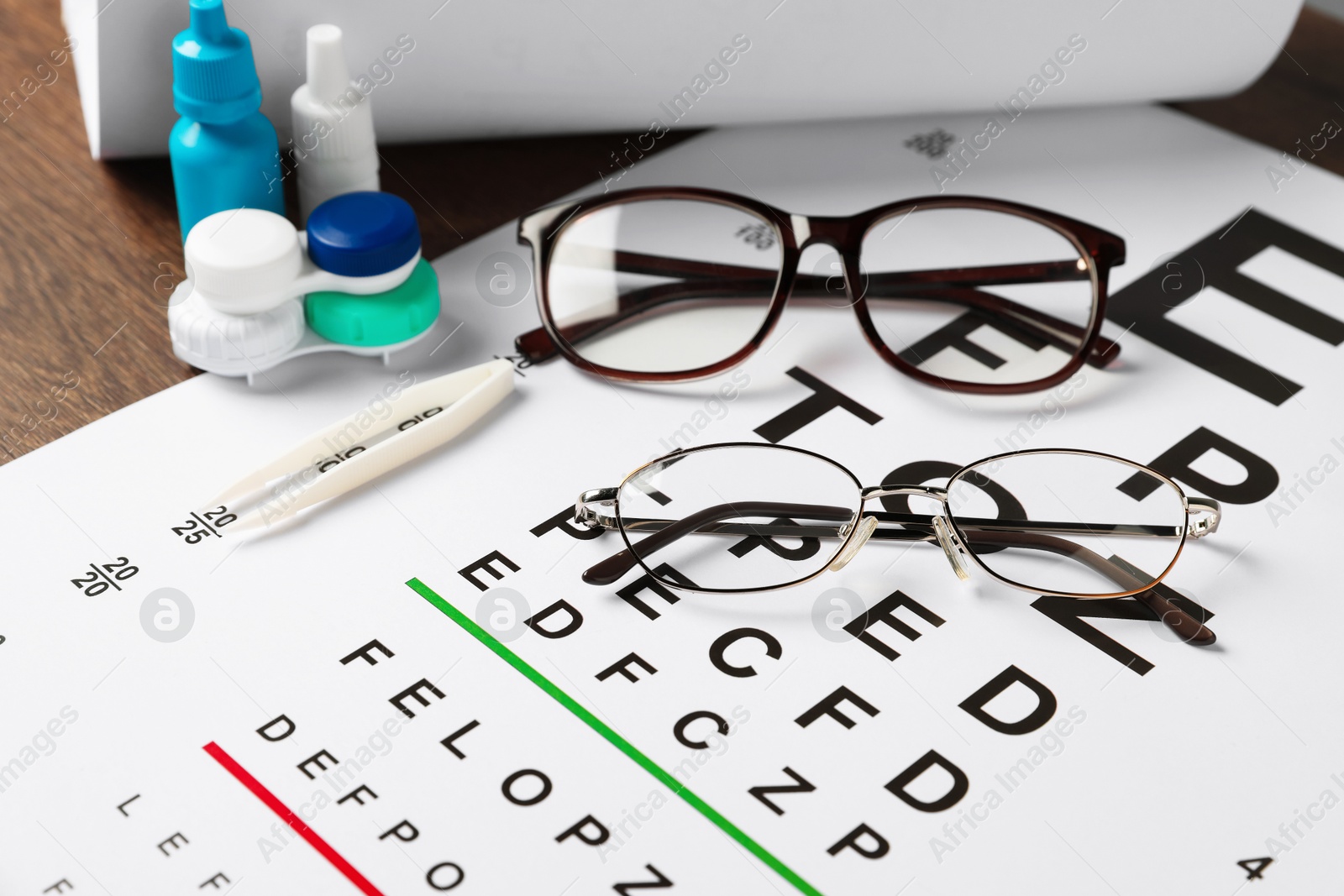 Photo of Vision test chart, glasses, tweezers, bottles of medical drops and lenses on wooden table, closeup