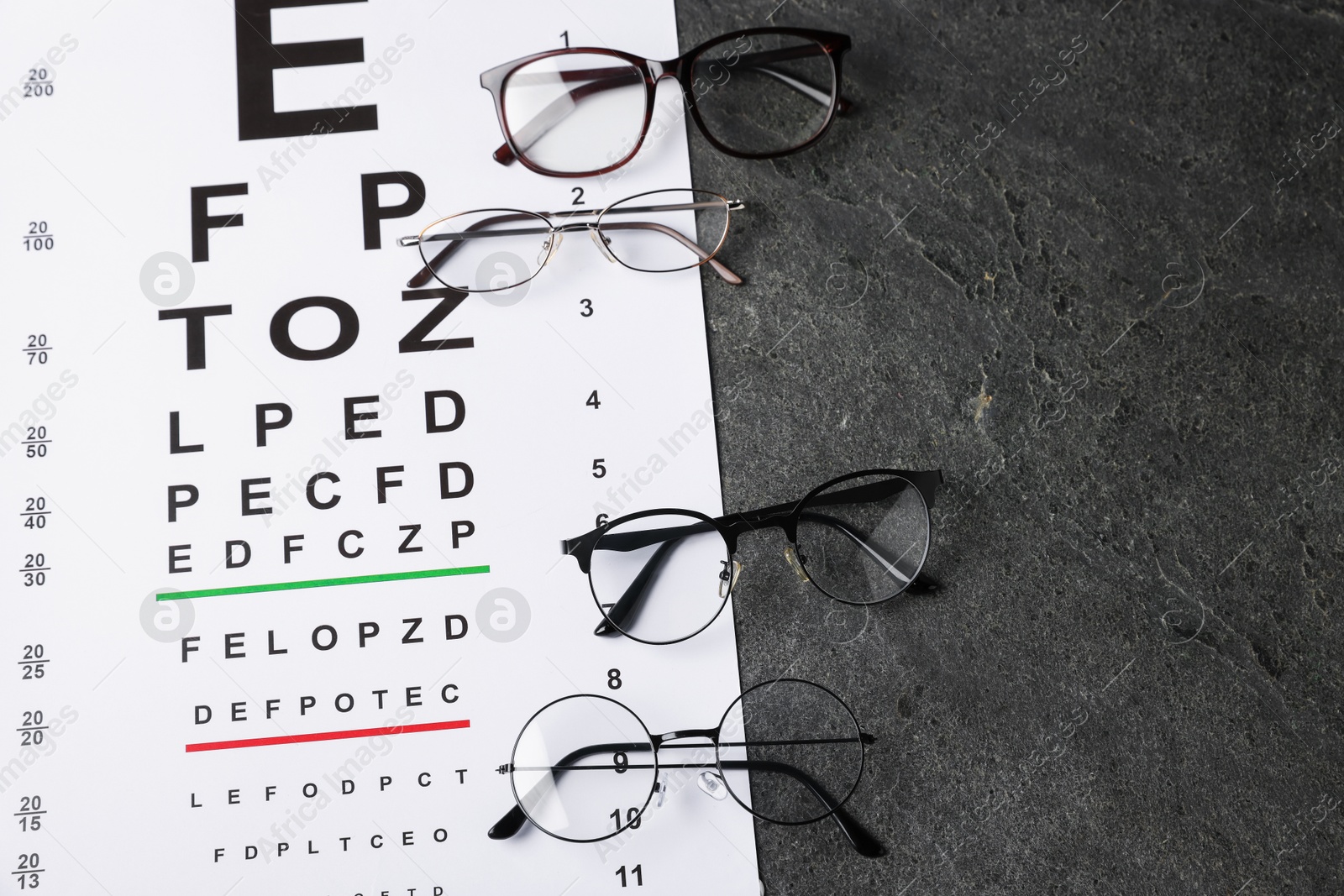 Photo of Vision test chart and glasses on grey table, above view. Space for text