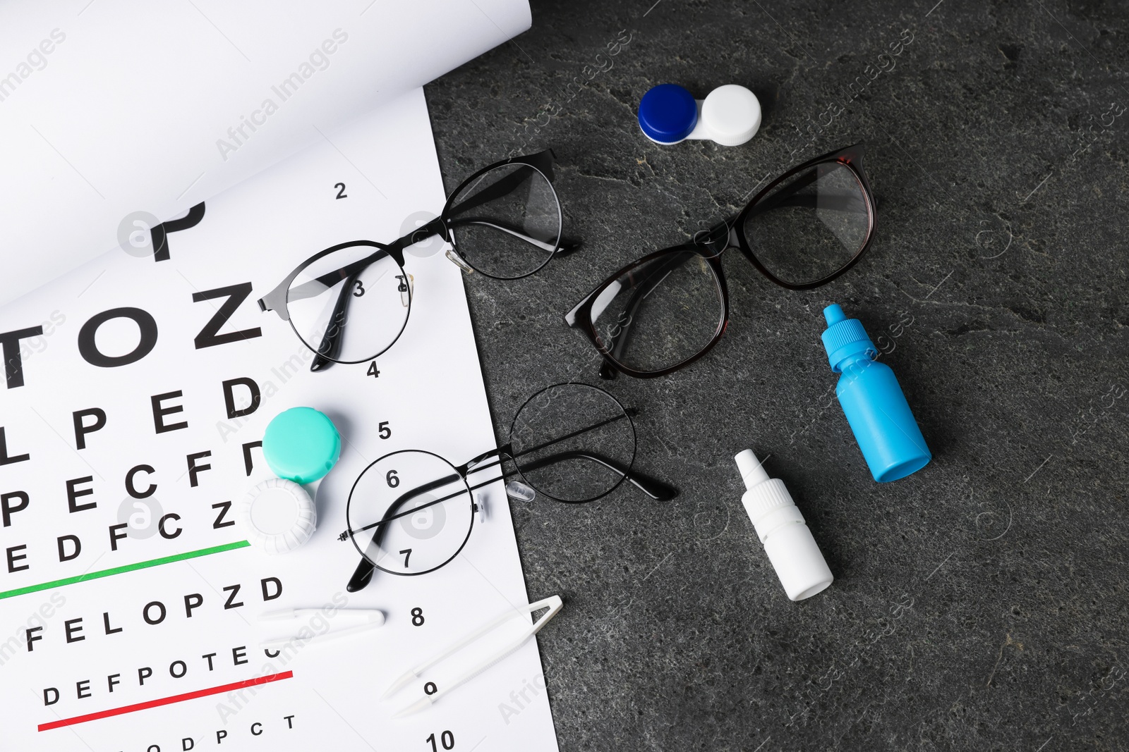 Photo of Vision test chart, glasses, tweezers, lenses and bottles of medical drops on grey table, flat lay