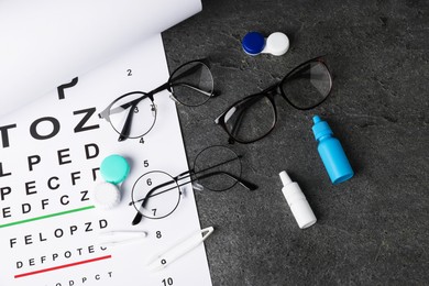 Photo of Vision test chart, glasses, tweezers, lenses and bottles of medical drops on grey table, flat lay