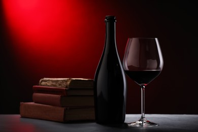 Photo of Tasty wine and stacked books on dark table in red light, closeup