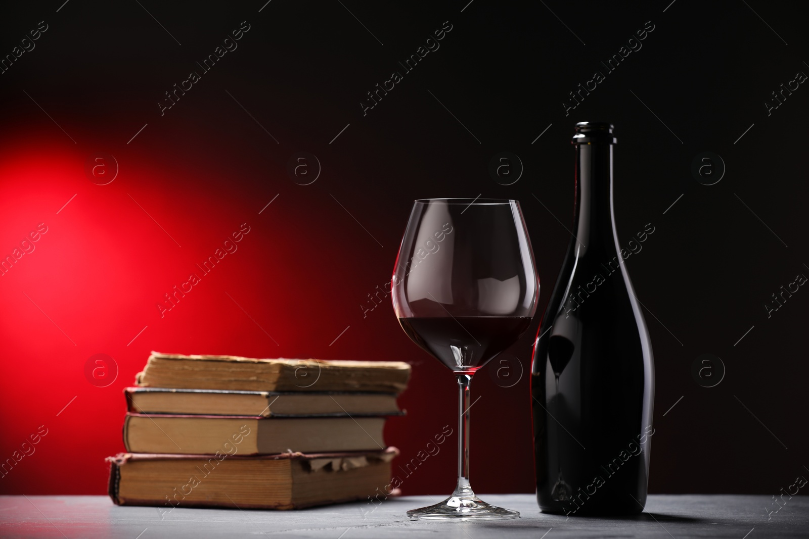 Tasty wine and stacked books on grey table in red light, closeup Photo of Tasty wine and stacked books on grey table in red light, closeup
