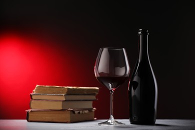 Photo of Tasty wine and stacked books on grey table in red light, closeup