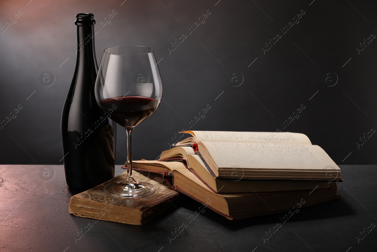 Tasty wine and books on dark textured table in color light, closeup Photo of Tasty wine and books on dark textured table in color light, closeup