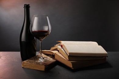 Photo of Tasty wine and books on dark textured table in color light, closeup