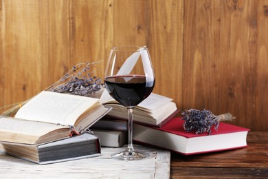 Photo of Red wine in glass, lavender flowers and books on wooden table, closeup