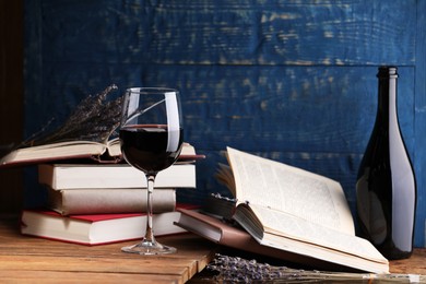 Photo of Red wine in glass, bottle, lavender flowers and books on wooden table against blue background, closeup