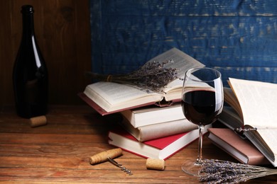 Photo of Red wine in glass, lavender flowers and books on wooden table against blue background