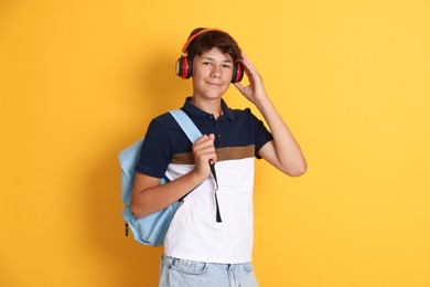 Photo of Teenage boy in headphones with backpack on orange background