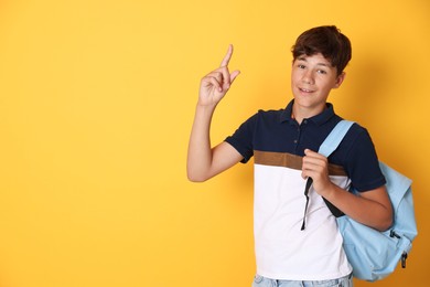 Photo of Teenage boy with backpack pointing at something on orange background, space for text