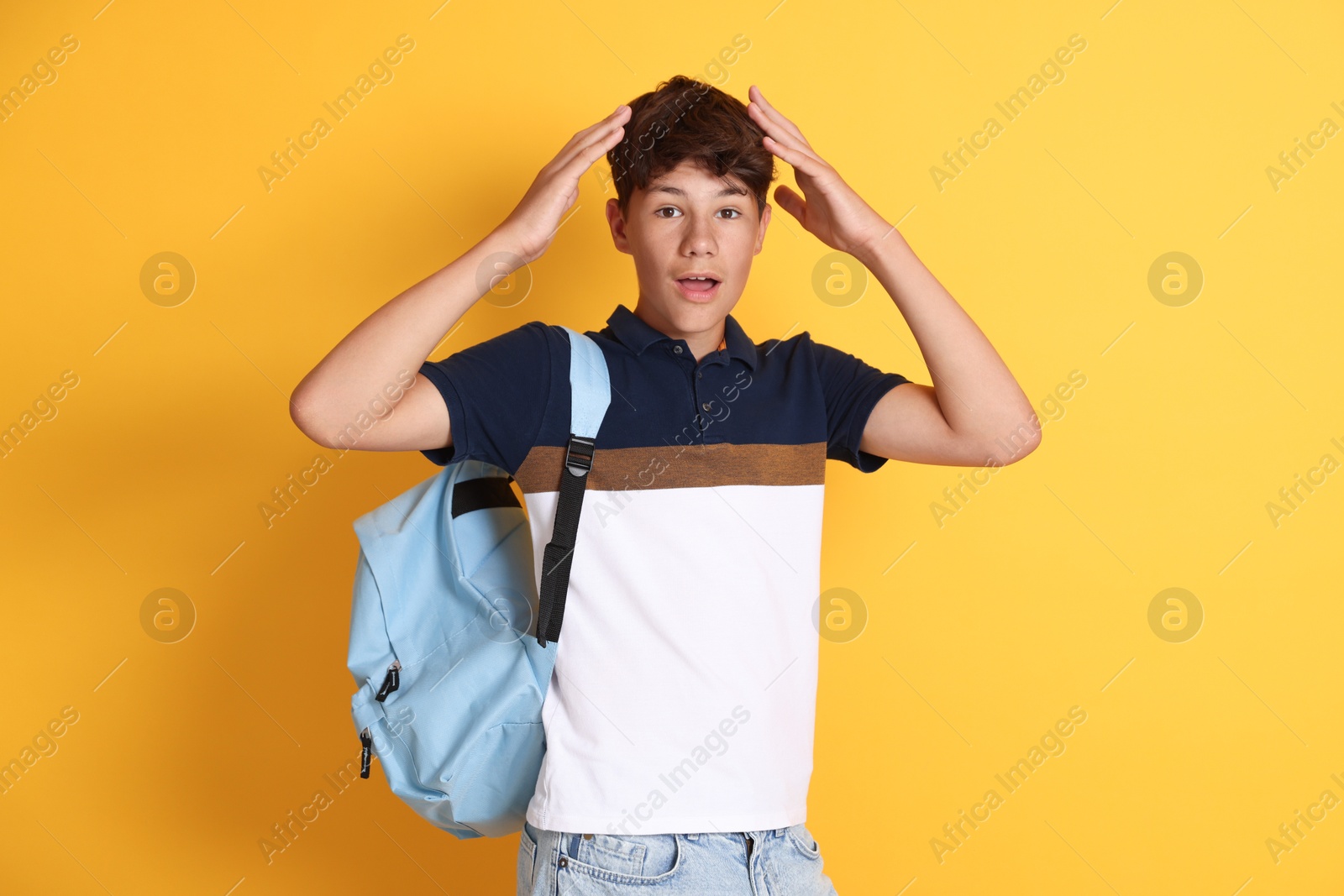 Teenage boy with backpack on orange background Photo of Teenage boy with backpack on orange background