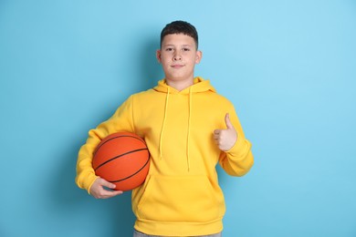 Photo of Teenage boy with basketball ball showing thumbs up on light blue background