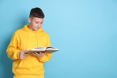 Photo of Teenage boy reading book on light blue background, space for text