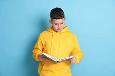 Photo of Teenage boy reading book on light blue background