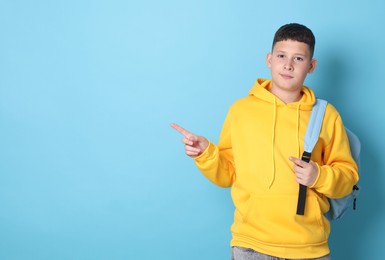 Photo of Teenage boy with backpack pointing at something on light blue background, space for text