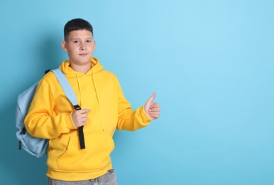 Photo of Teenage boy with backpack showing thumbs up on light blue background, space for text