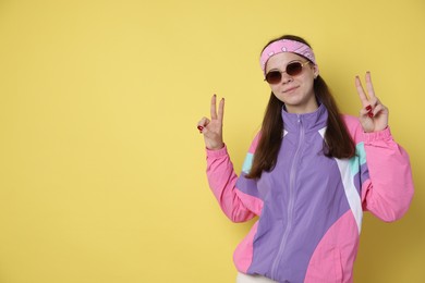 Photo of Teenage girl in sunglasses showing peace sign on yellow background, space for text