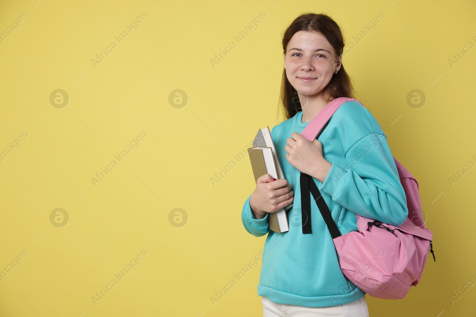 Teenage girl with backpack and books on yellow background, space for text Photo of Teenage girl with backpack and books on yellow background, space for text