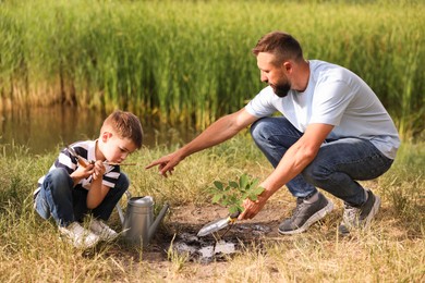 Photo of Father and his son planting tree into soil outdoors