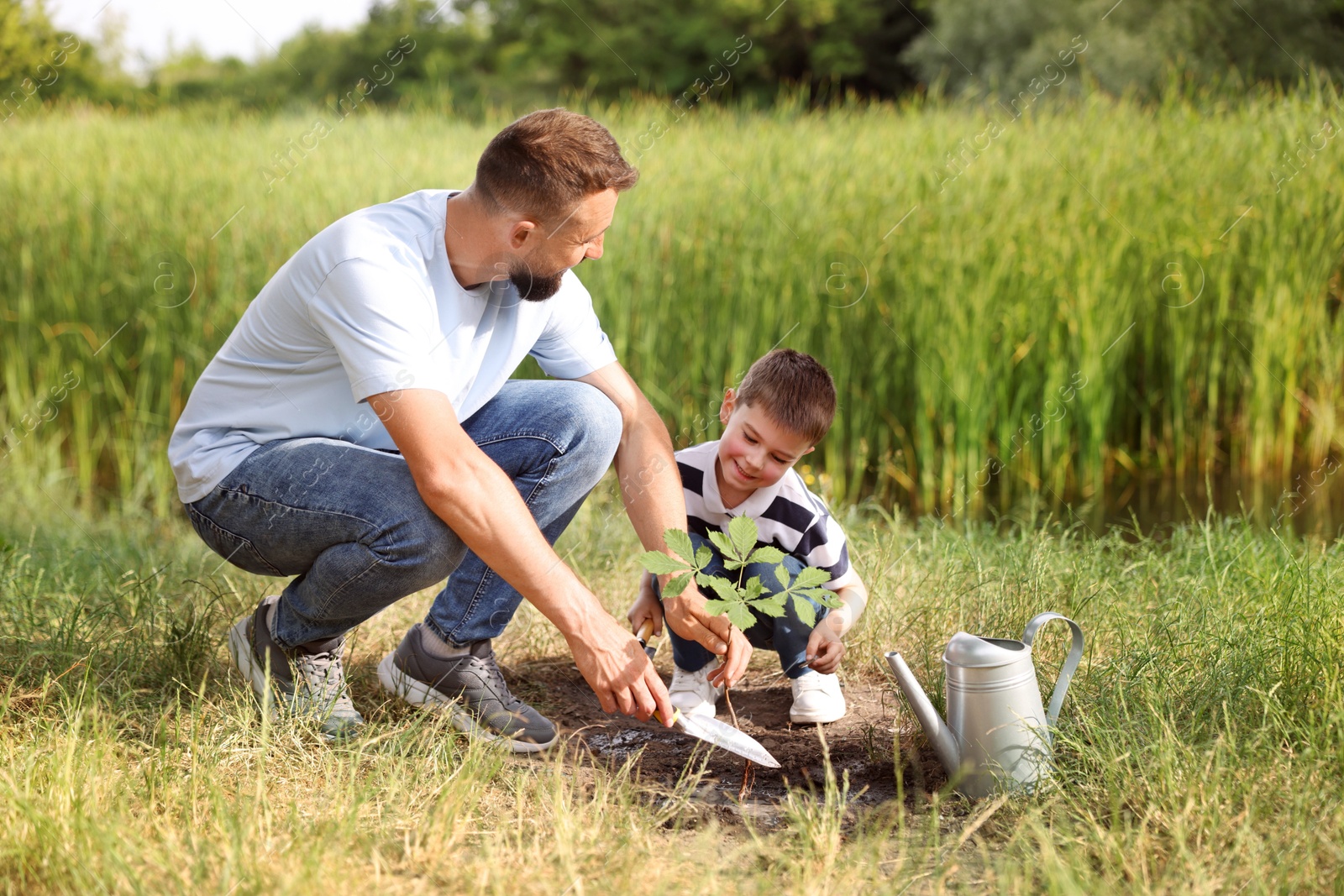 Photo of Father and his son planting tree into soil outdoors