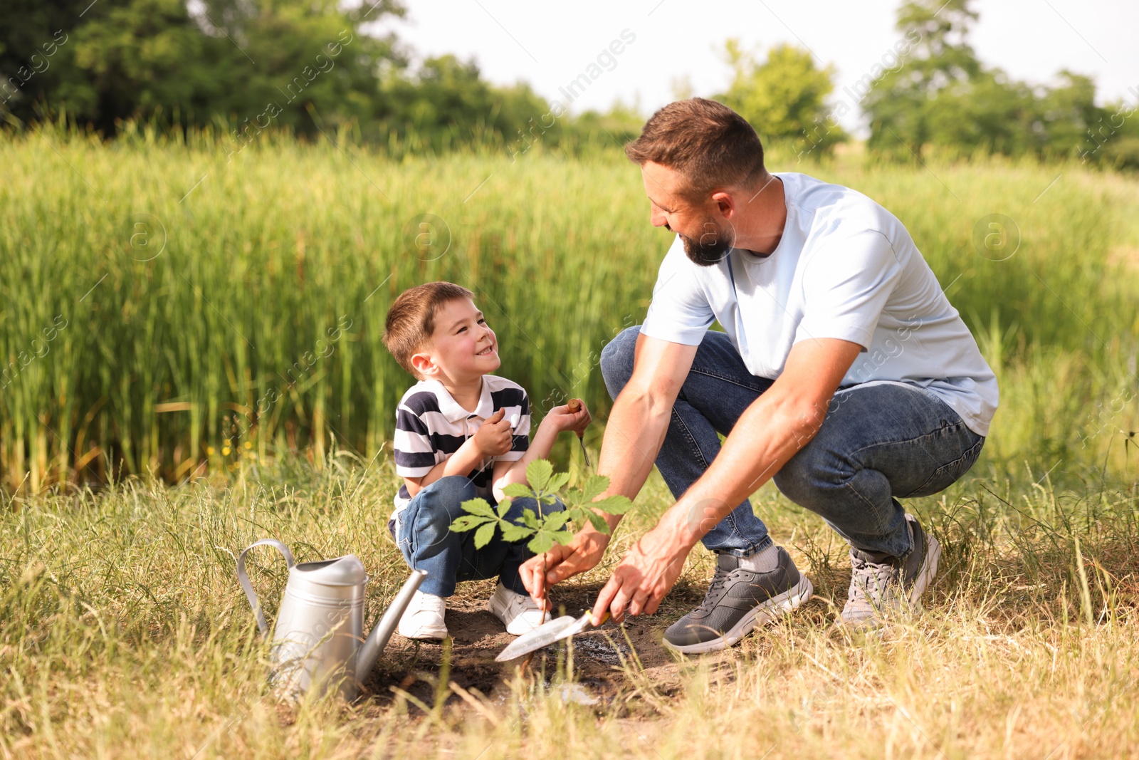 Father and his son planting tree into soil outdoors Photo of Father and his son planting tree into soil outdoors