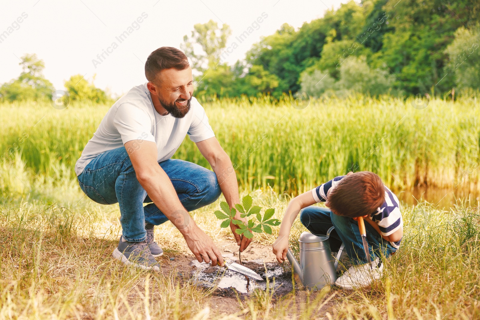 Photo of Father and his son planting tree into soil outdoors
