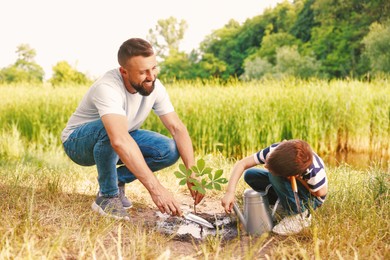 Photo of Father and his son planting tree into soil outdoors