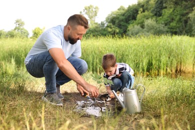 Photo of Father and his son planting tree into soil outdoors