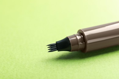 Photo of One liquid eyebrow pencil on green background, closeup. Space for text