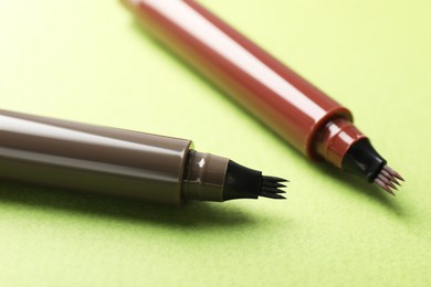 Photo of Liquid eyebrow pencils on green background, closeup